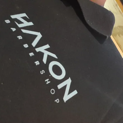 Capa de corte preta com o logo Hakon Barbershop