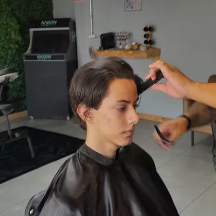 Jovem cortando o cabelo com o fliperama Hakon ao fundo