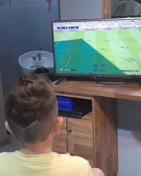 Cliente jogando futebol no videogame enquanto corta o cabelo